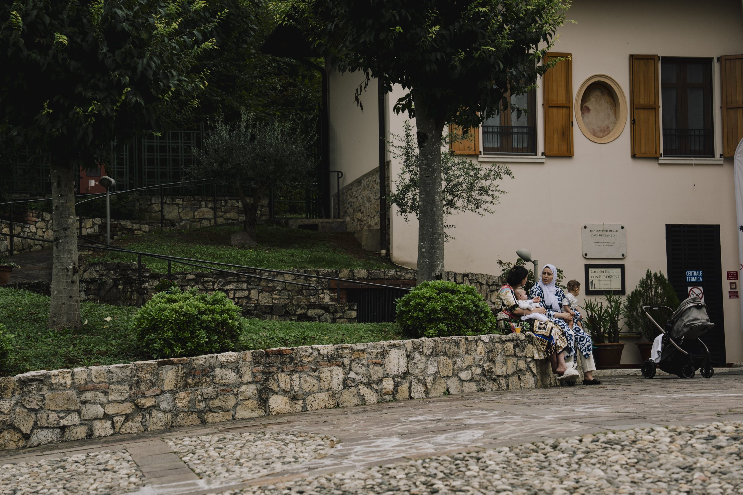 Due donne con i figli in braccio, che parlano sedute nel cortile