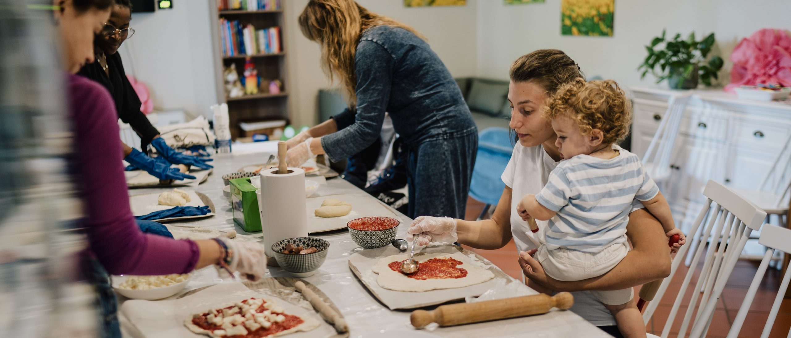 Madre che prepara la pizza con la propria figlia in braccio